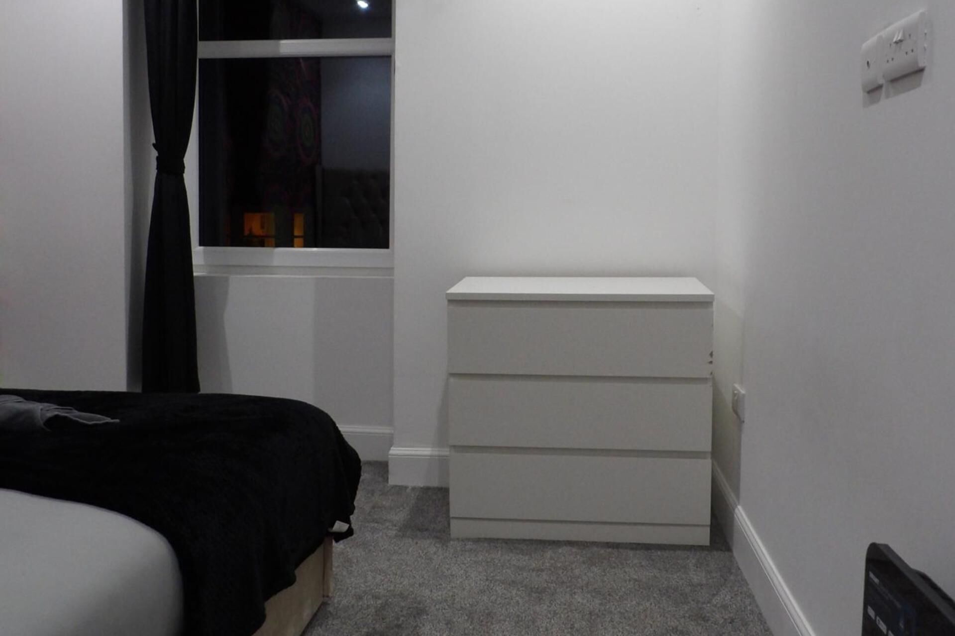 A bedroom with a bed, a white dresser, and a window with curtains.