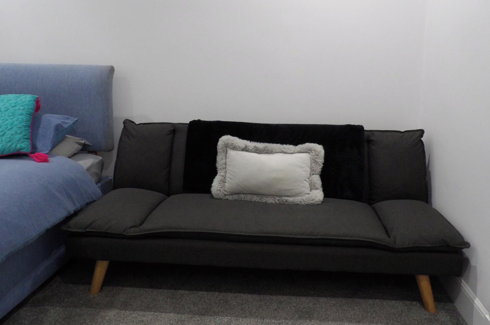 A dark grey sofa with a white fluffy pillow and a black throw blanket.