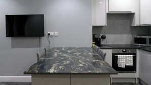 A modern kitchen with a marble countertop, built-in oven, microwave, and a flat-screen TV mounted on the wall. - 2bed Apt Sleeps 4-near Meadows Park, Parking, Wifi (Edinburgh)