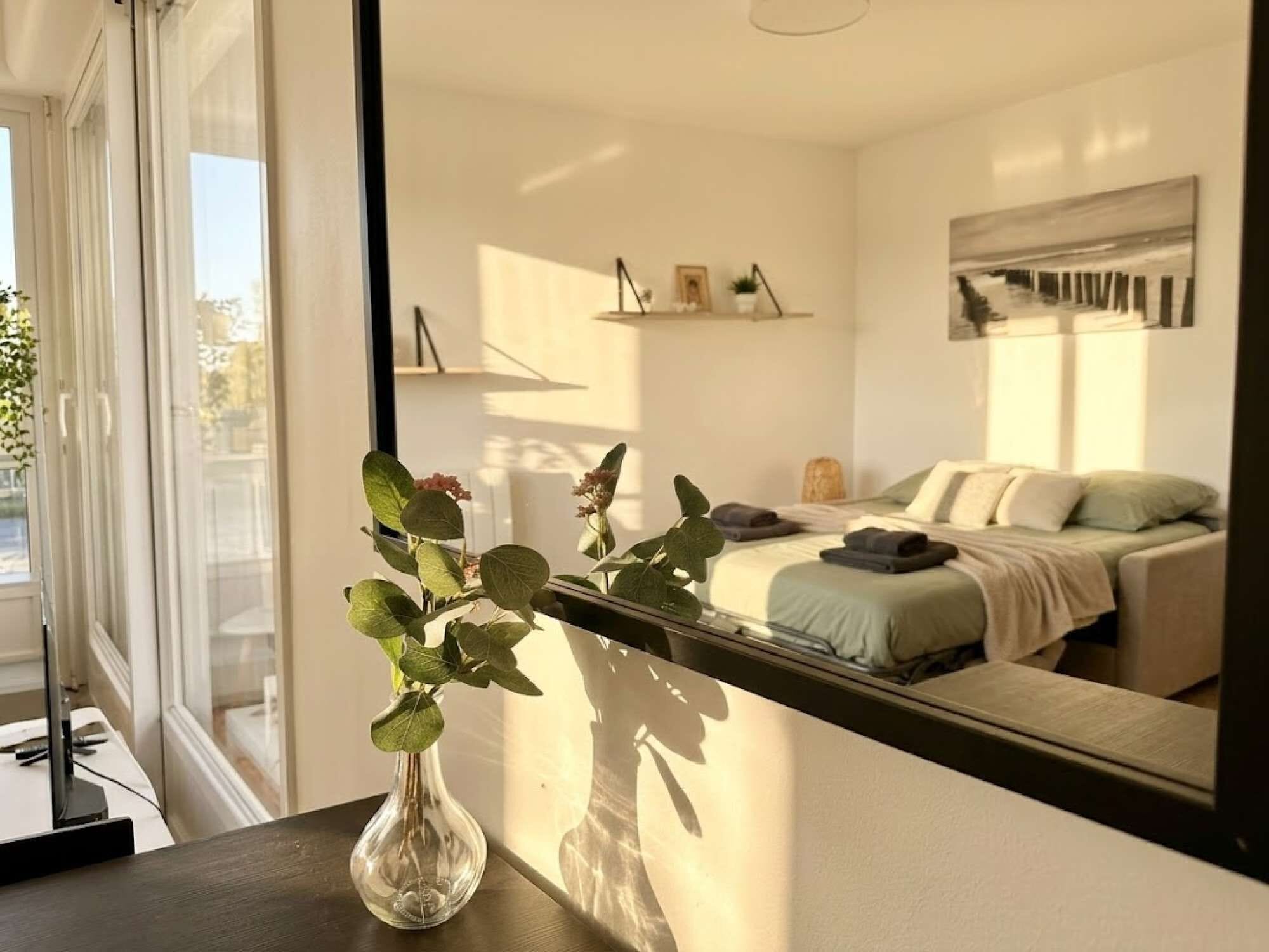 A bedroom with a bed, bedside table, and a mirror reflecting the room.