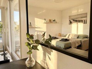 A bedroom with a bed, bedside table, and a mirror reflecting the room.