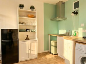 A compact kitchen with a black refrigerator, white cabinets, a dishwasher, and a washing machine.