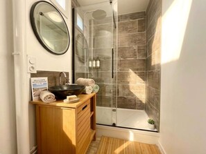 A modern bathroom with a glass-enclosed shower, a wooden vanity with a sink, and a mirror.