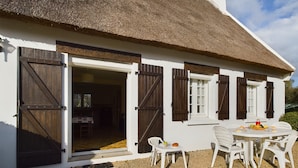 A white house with a thatched roof, wooden shutters, and a dining area with white chairs and a table set with food. - -HANSEL- Belle Chaumière à Kerascöet (Névez)