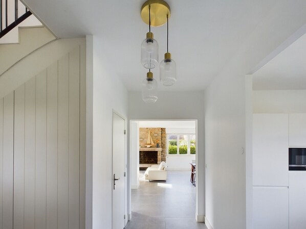Een modern interieur met een trap, een hal die leidt naar een zithoek met een open haard, en een eetgedeelte.