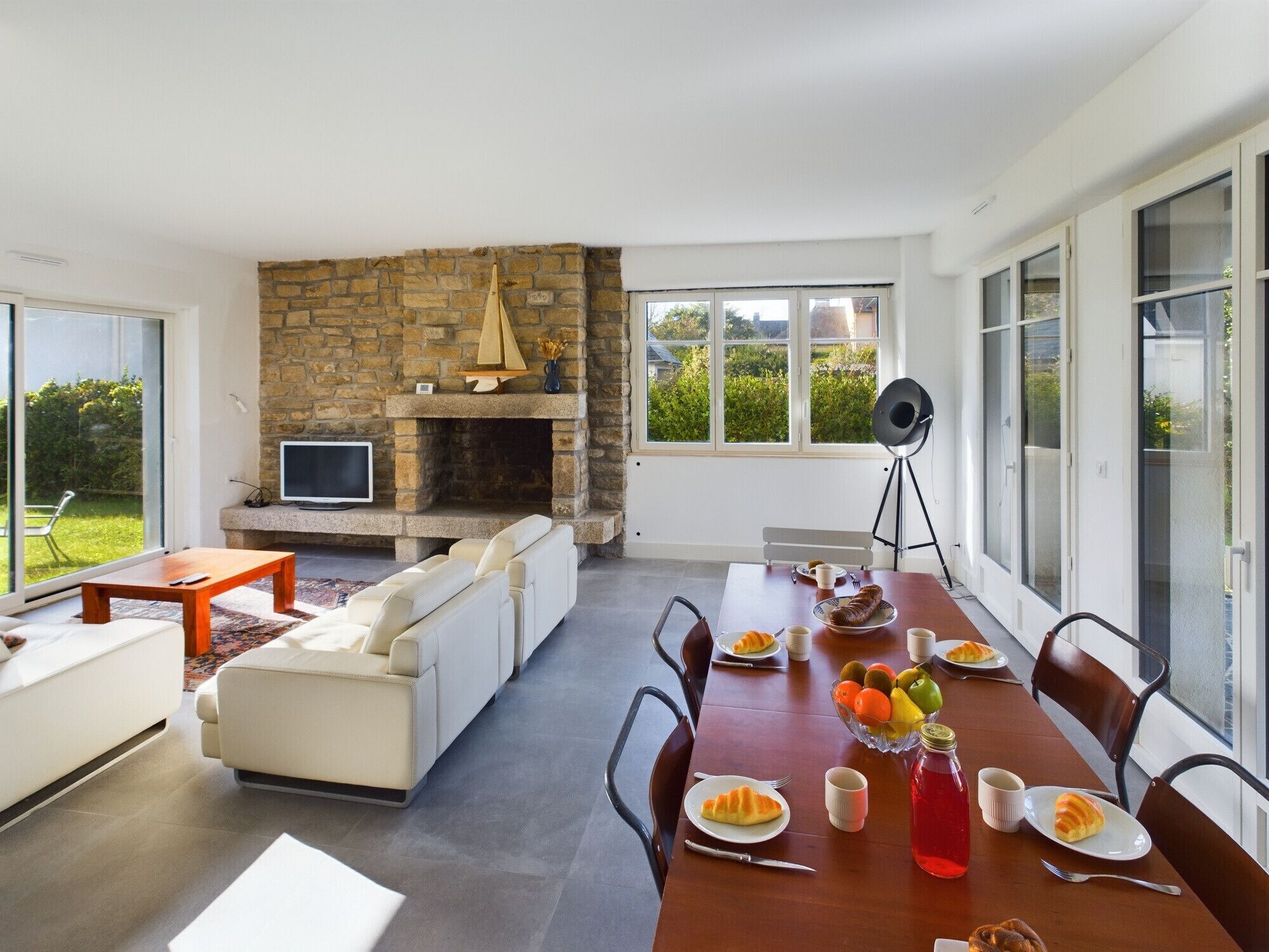 A modern living room with a stone fireplace, a dining table set for a meal, and a sofa.