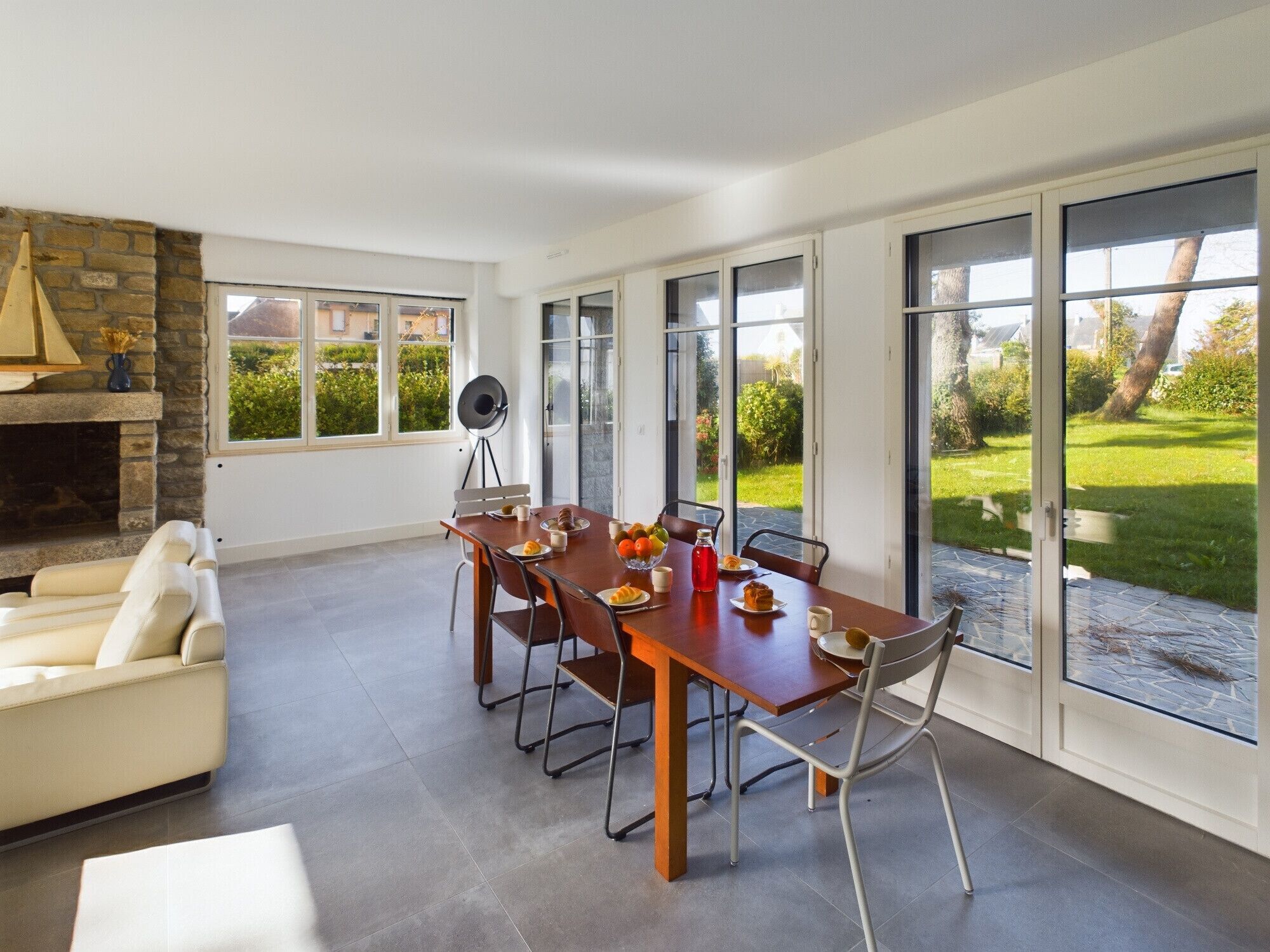 A modern dining area with a stone fireplace, a round table with chairs, and large sliding glass doors offering a view of a garden.