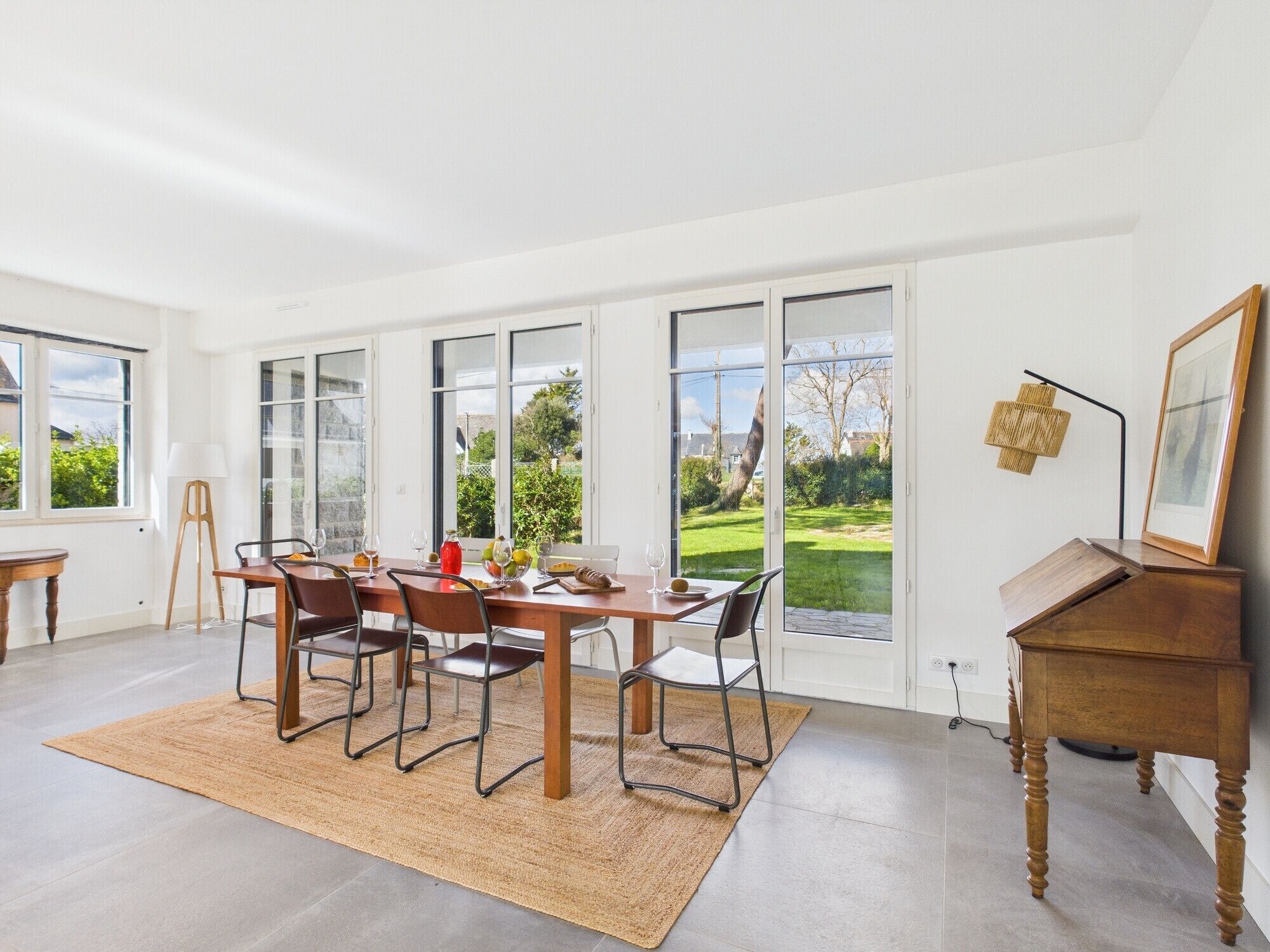 A dining area with a table set for six, large windows, and a view of a green landscape.