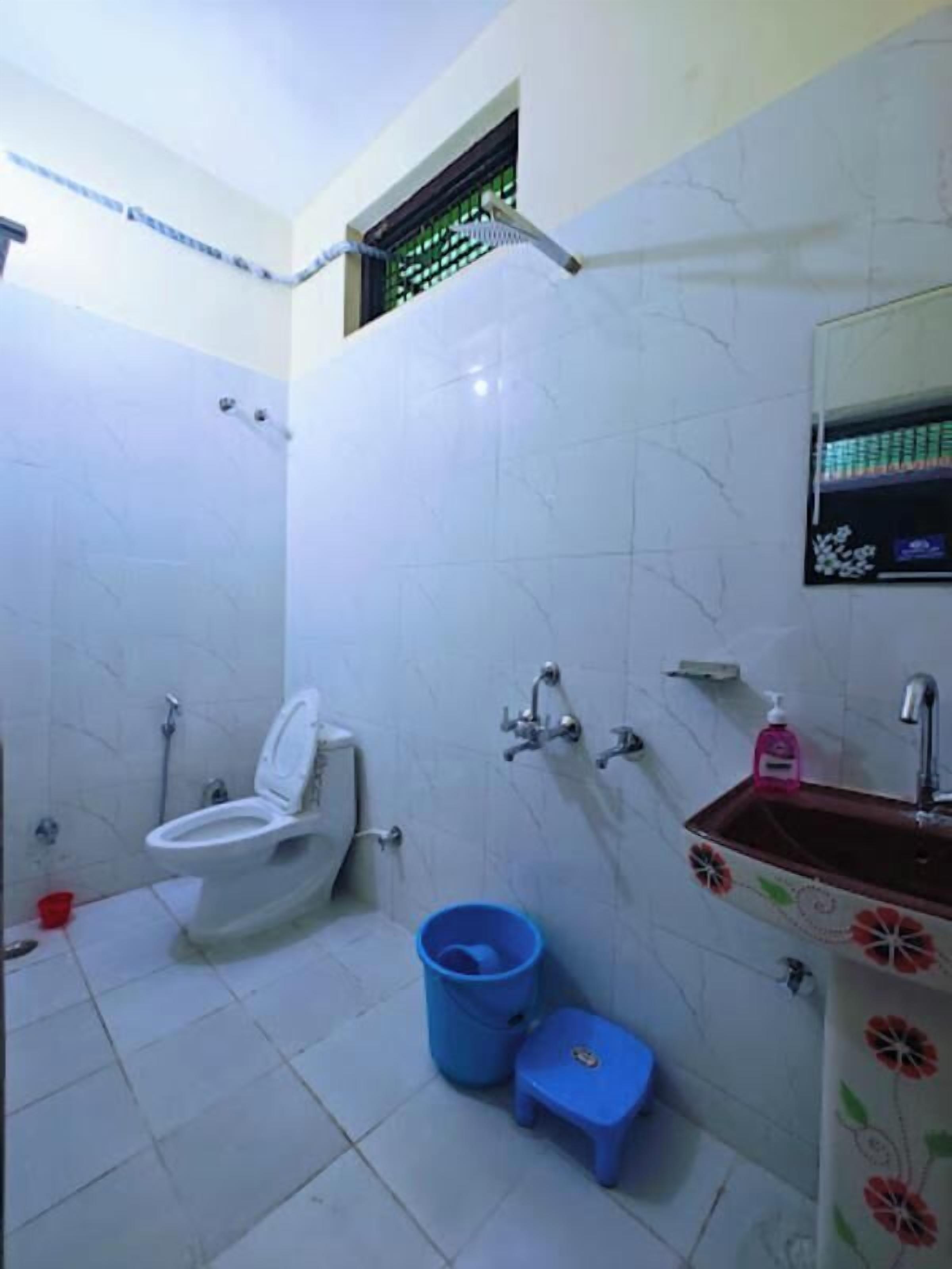 A bathroom with a toilet, sink, and blue bucket.