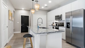 A modern kitchen with a central island, stainless steel appliances, and pendant lighting. - Modern 2-Bed Apartment Complex - Owasso, OK (Owasso)