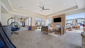A spacious outdoor lounge area with seating arrangements, a hanging chair, and a flat-screen TV mounted on a brick wall. - Modern 2-Bed Apartment Complex - Owasso, OK (Owasso)