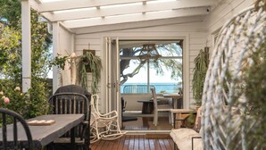 Un patio al aire libre con piso de madera, sillas de mimbre blanco, una mesa y vista al mar.