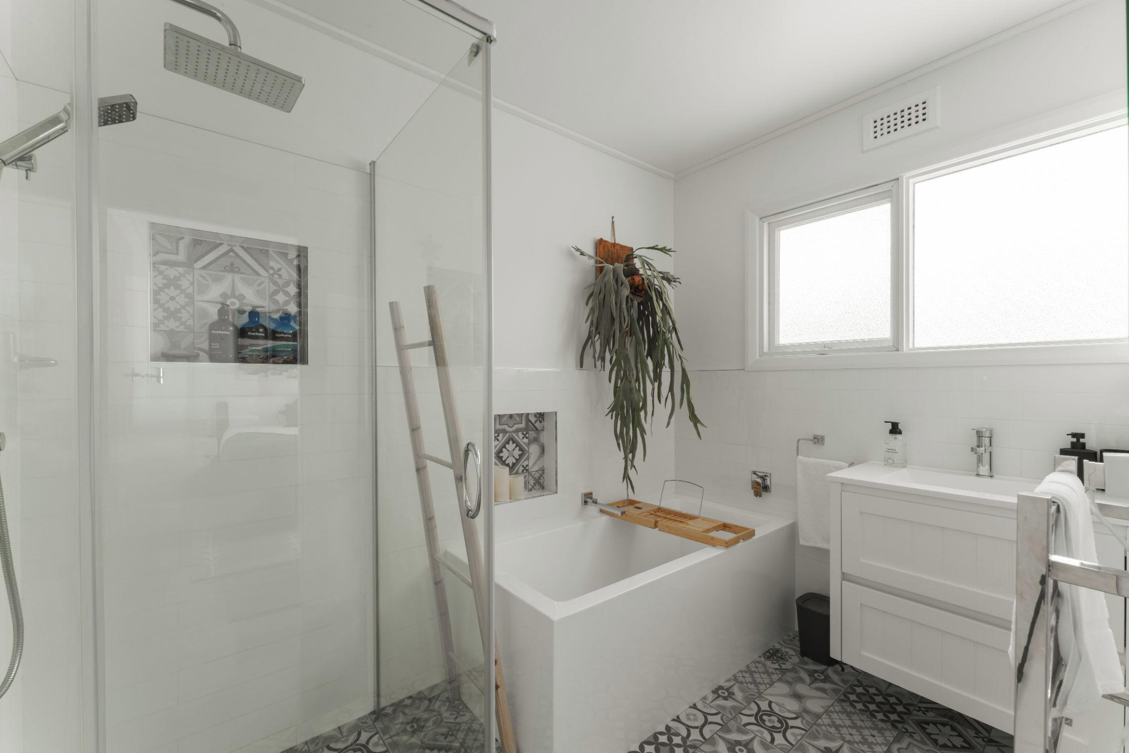 A modern bathroom with a glass shower enclosure, a freestanding bathtub, and a large window providing natural light.