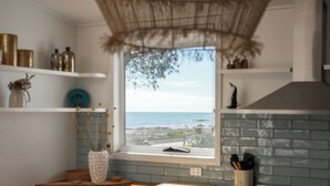 Una cocina con vista al mar, una ventana con vistas y un estante con objetos decorativos.