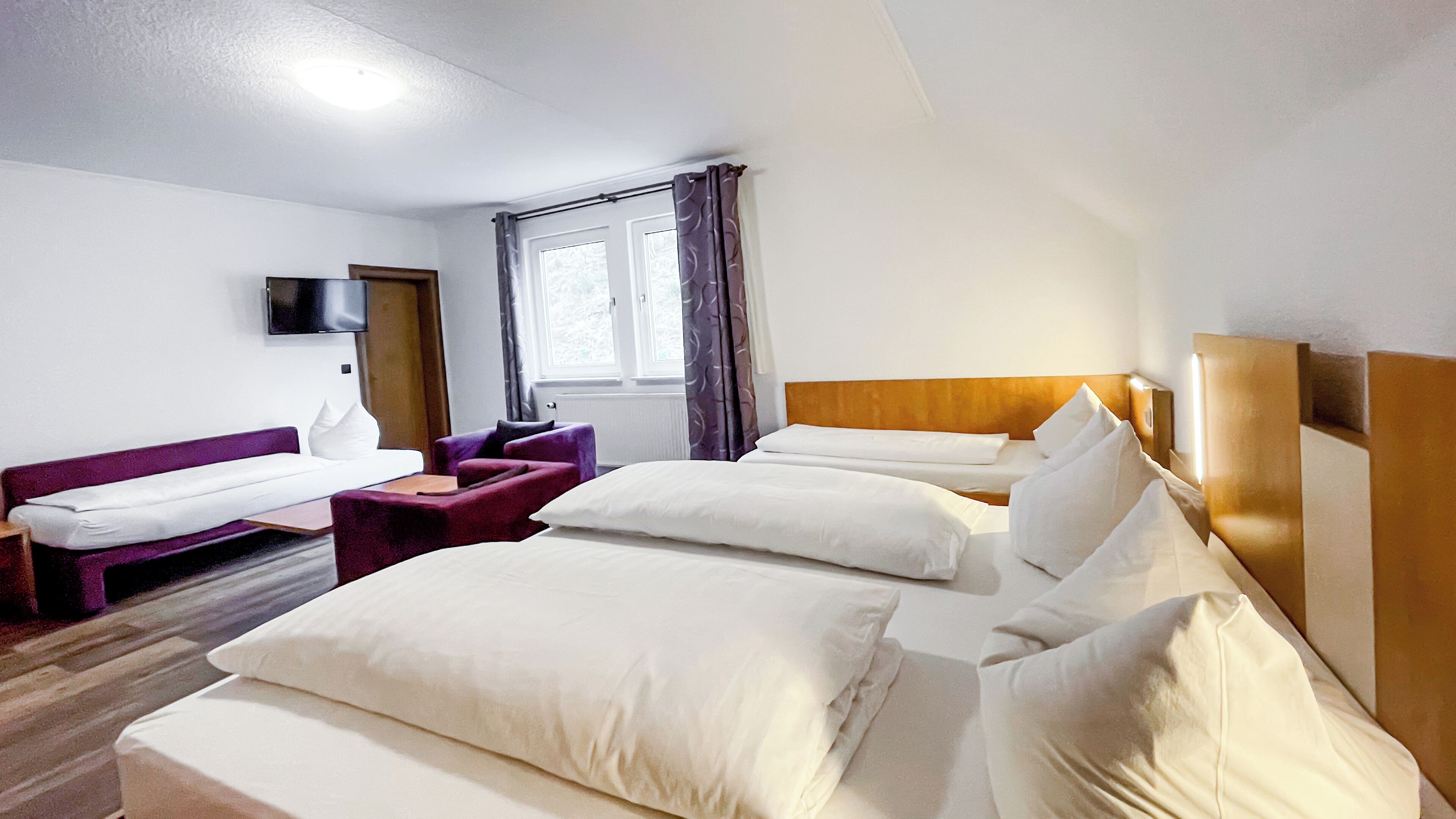 A hotel room with two beds, a sofa, a chair, a flat-screen TV, and a window with curtains.