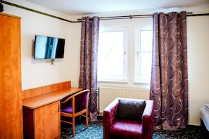 A room with a wooden desk, a red chair, a television, and a window with curtains.