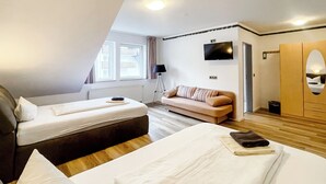 Habitación de hotel con dos camas, un sofá, un televisor y un armario.