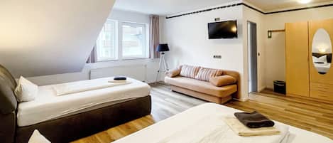 Habitación de hotel con dos camas, un sofá, un televisor y un armario.