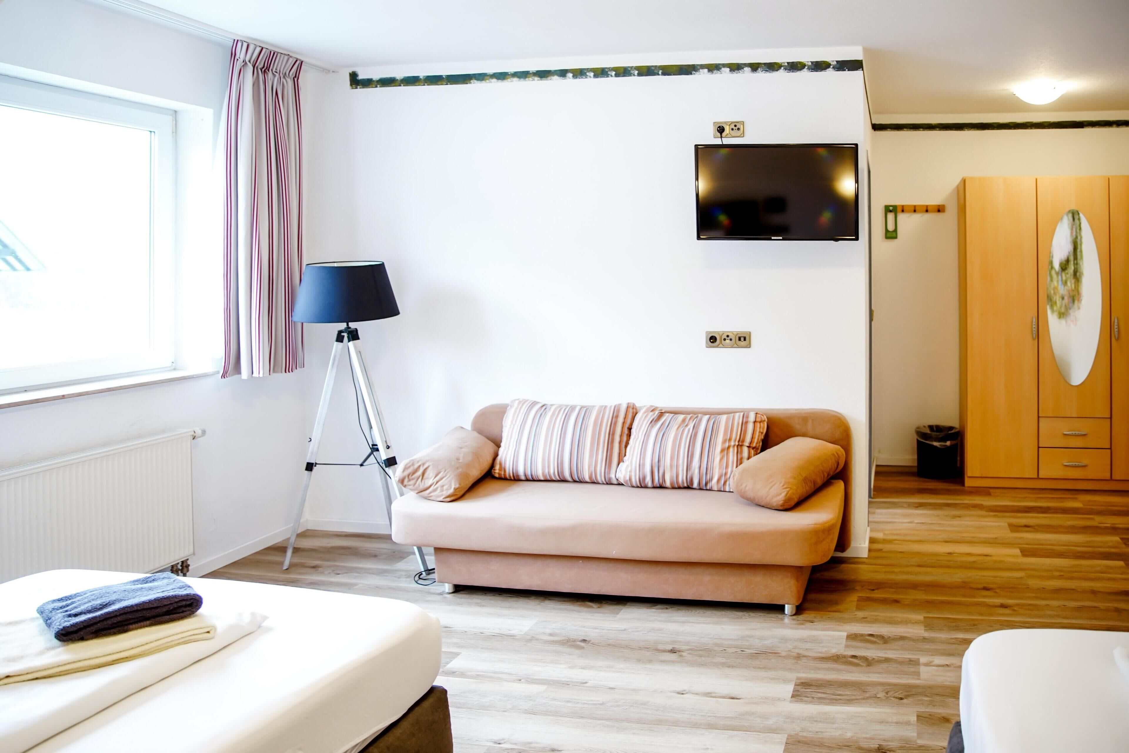 Una habitación con cama, sofá, lámpara de pie, televisor en la pared y armario.