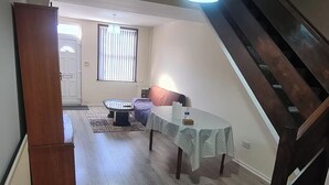 Une pièce comprenant un lit, une petite table avec une chaise, une fenêtre avec des stores et un escalier.
