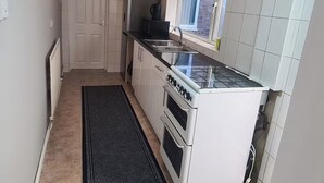Une cuisine de taille réduite avec des meubles blancs, un plan de travail noir, une cuisinière et une fenêtre.