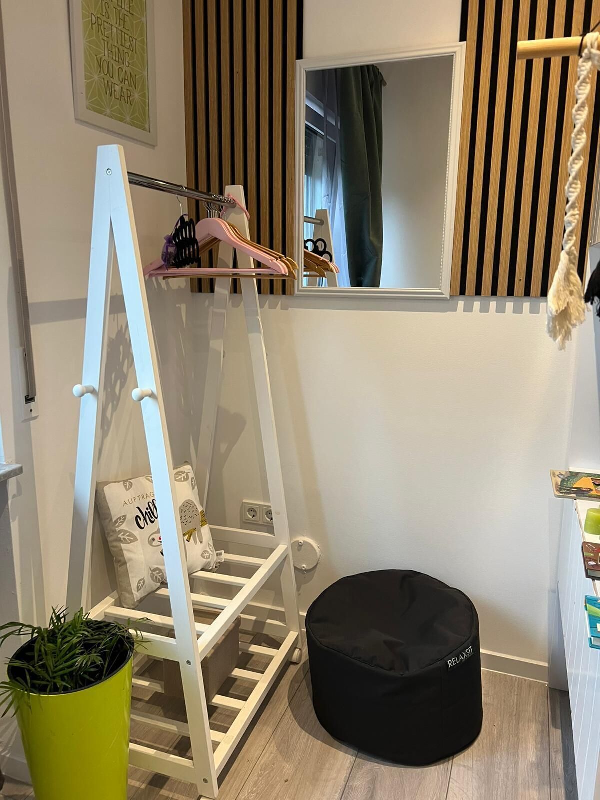 A room with a white ladder, a black bean bag, a green plant, and a mirror with a wooden slat design.