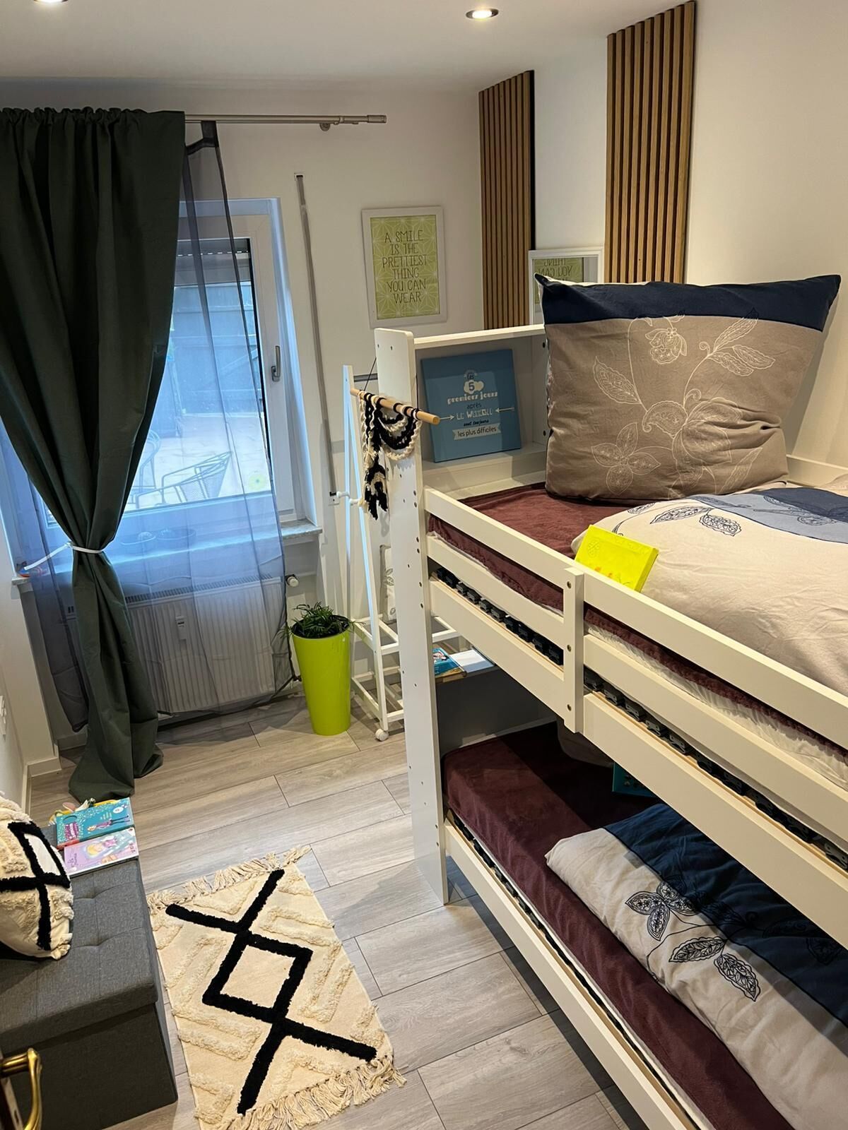Habitación con literas, una ventana, una planta pequeña y una frase inspiradora en la pared.