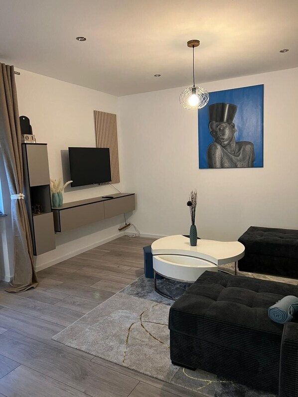 Una sala de estar moderna con una televisión de pantalla plana, un cuadro, una mesa de centro redonda y un sofá negro.