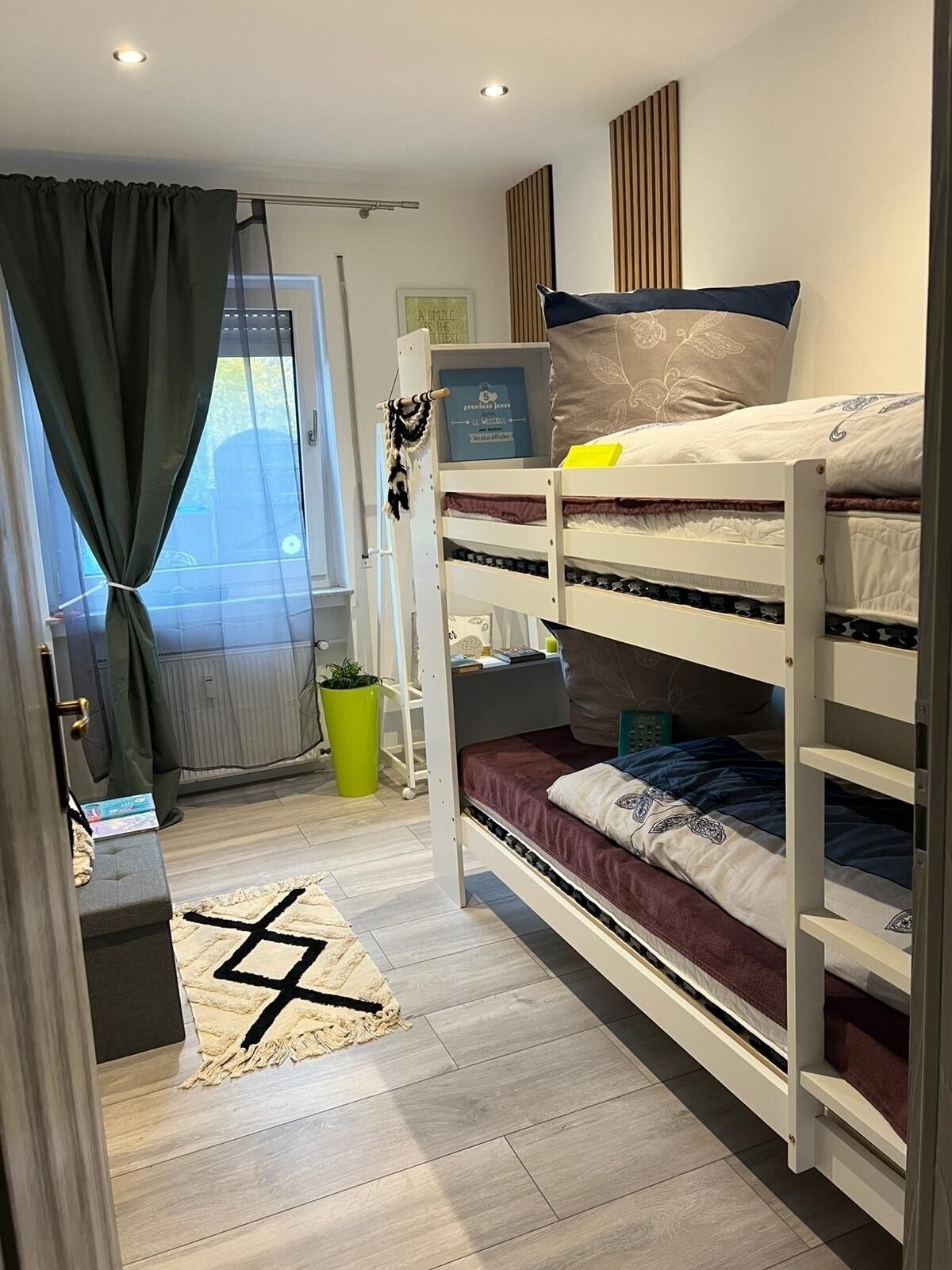 Een kleine kamer met stapelbedden, een bureau, een potplant en uitzicht op het landschap.