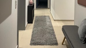 Un pasillo moderno con alfombra gris, un sofá y una consola negra con un florero.
