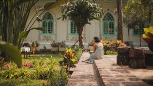 A woman sitting on a stone pathway in a garden with a building in the background. - Brij Casa Susegad, Goa - An Indo-Portuguese Villa (Loutolim)