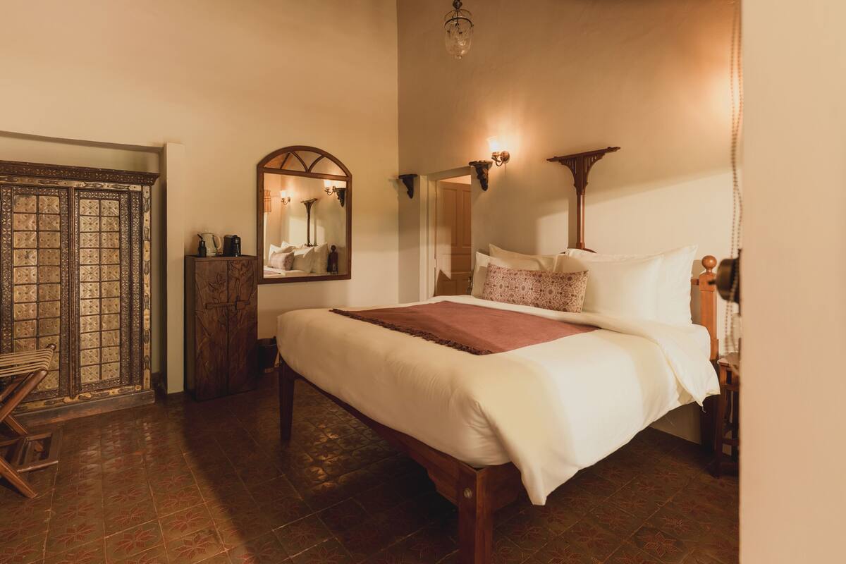 Een slaapkamer met een bed, een houten garderobe, een spiegel en een deur.