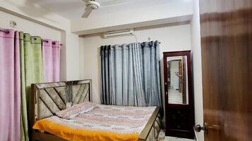 Quarto com cama, cortinas, ventoinha no teto e porta.