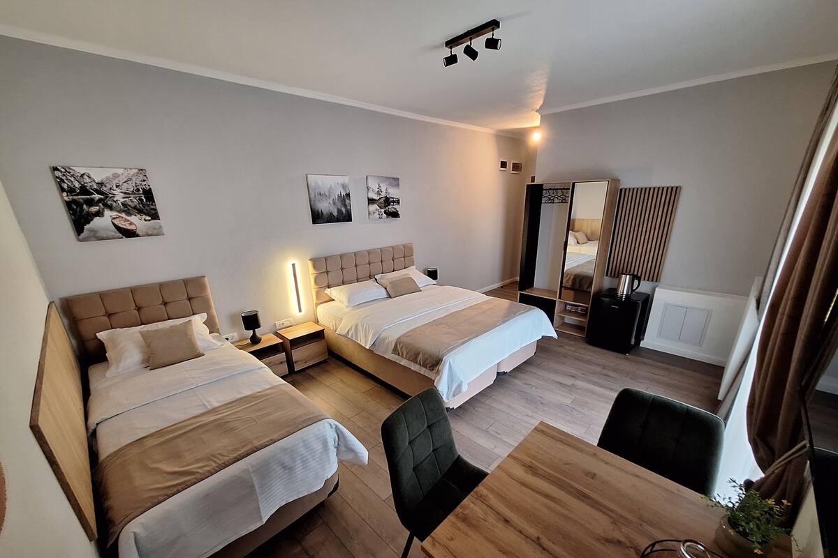 Une chambre d’hôtel avec deux lits, un bureau en bois, une chaise, un miroir et des œuvres d’art accrochées aux murs.