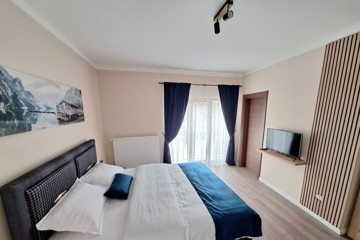 Une chambre à coucher avec un lit, une télévision, un tableau et une fenêtre avec des rideaux.