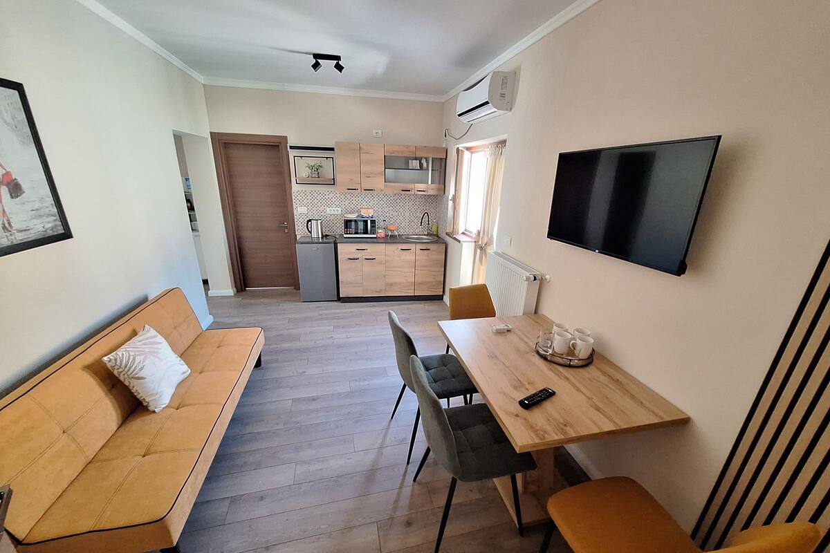 Un espace de vie compact comprenant un canapé, une table à manger, des chaises, un téléviseur, un coin cuisine et un radiateur.
