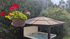 Un bain à remous installé sous une pergola, avec une suspension décorative remplie de fleurs.