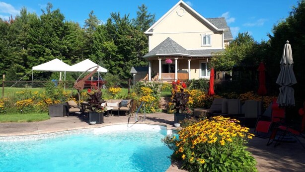 Un cadre résidentiel doté d’une piscine, d’un espace extérieur aménagé et d’une maison avec véranda.