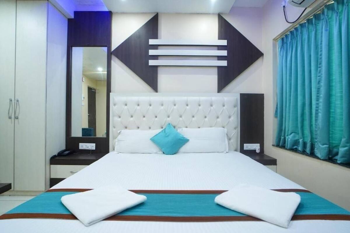 A hotel room with a large bed, a mirror, a bedside table, and a window with curtains.