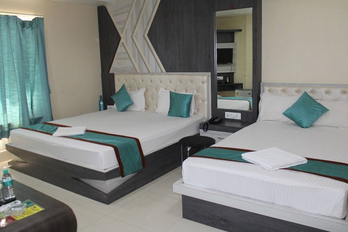 A hotel room with two beds, a mirror, a bedside table, and a small desk with a chair.