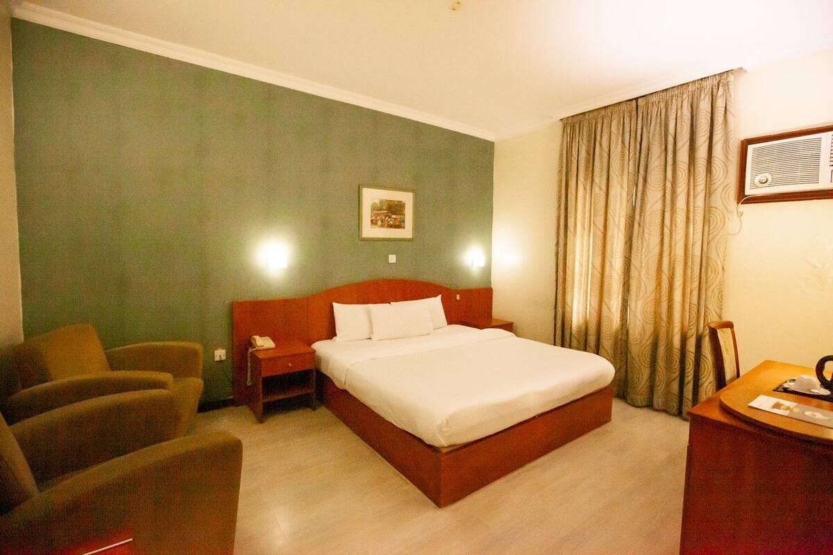 A hotel room with a single bed, a nightstand, a chair, a desk, and a large window with curtains.