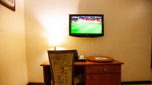 A hotel room with a desk, chair, lamp, and a television displaying a sports game. - Genesis Place  (Port Harcourt)