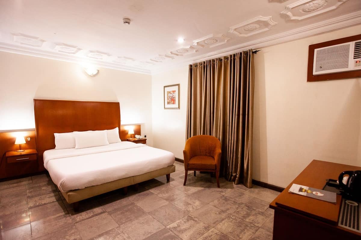 A hotel room with a large bed, a chair, a desk, and a wall-mounted air conditioning unit.