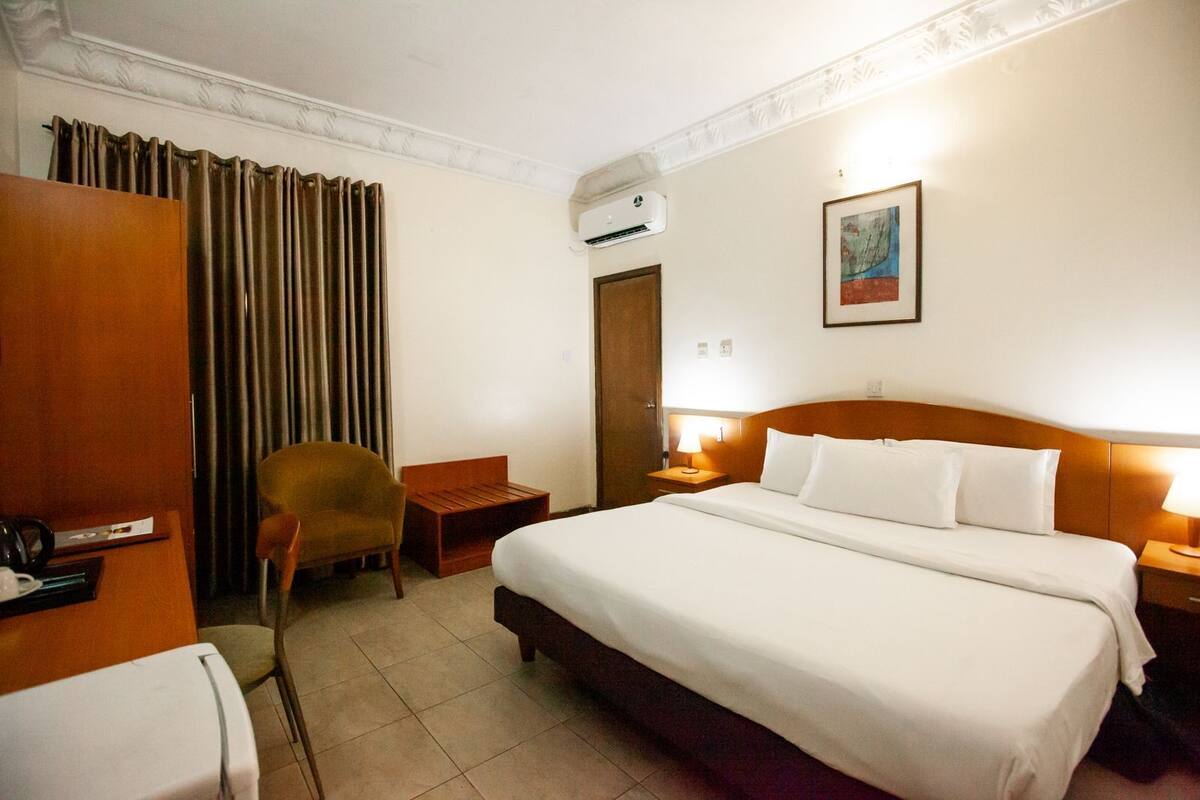 A hotel room with a large bed, a chair, a desk, and a wardrobe.