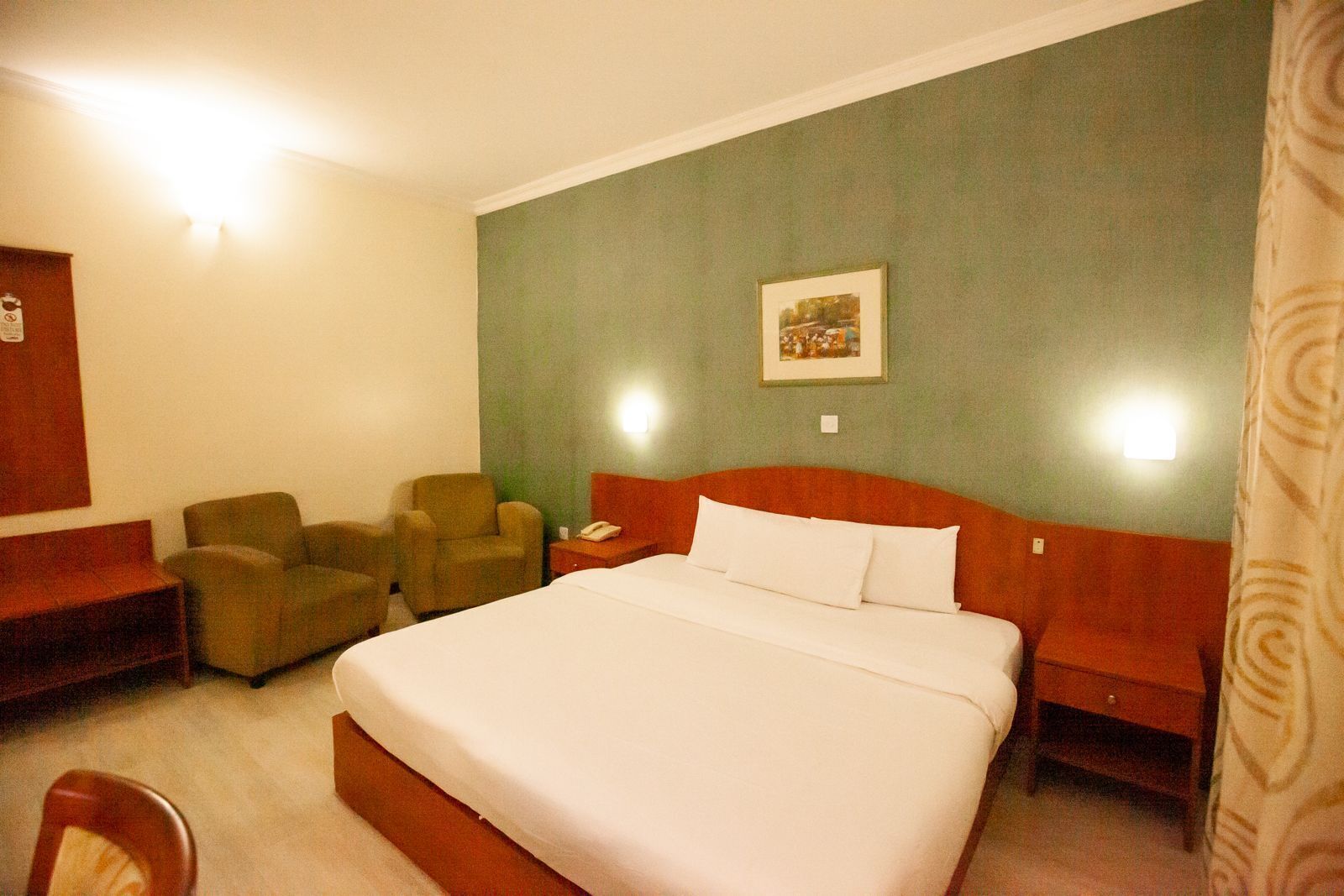 A hotel room with a large bed, two armchairs, a desk, and a nightstand.