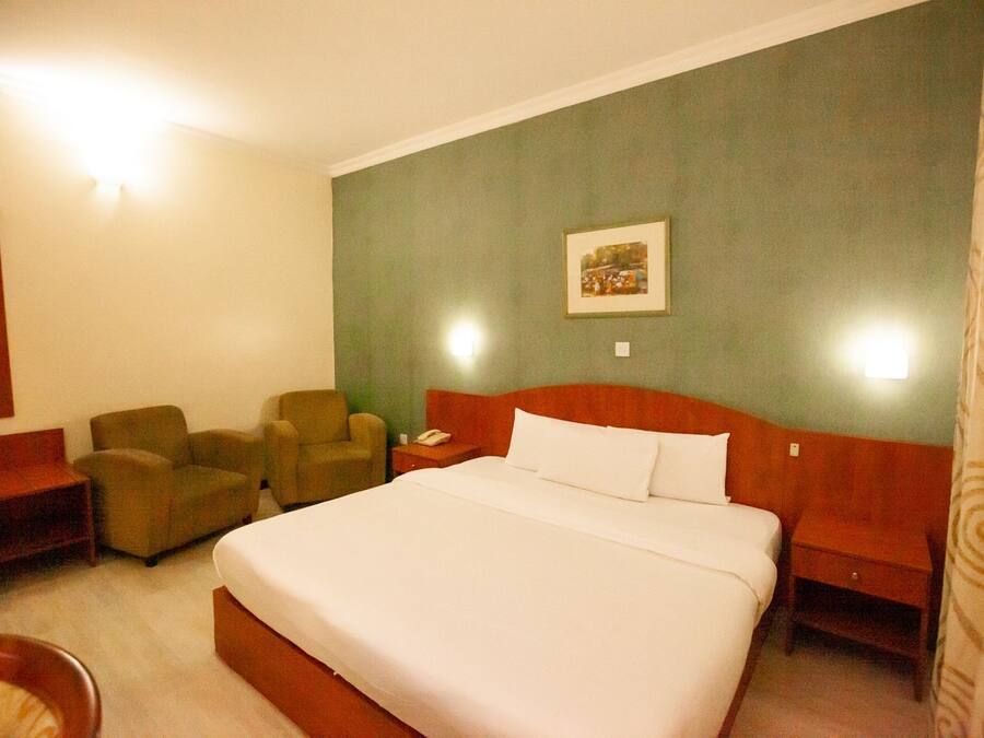A hotel room with a large bed, two armchairs, a desk, and a nightstand.