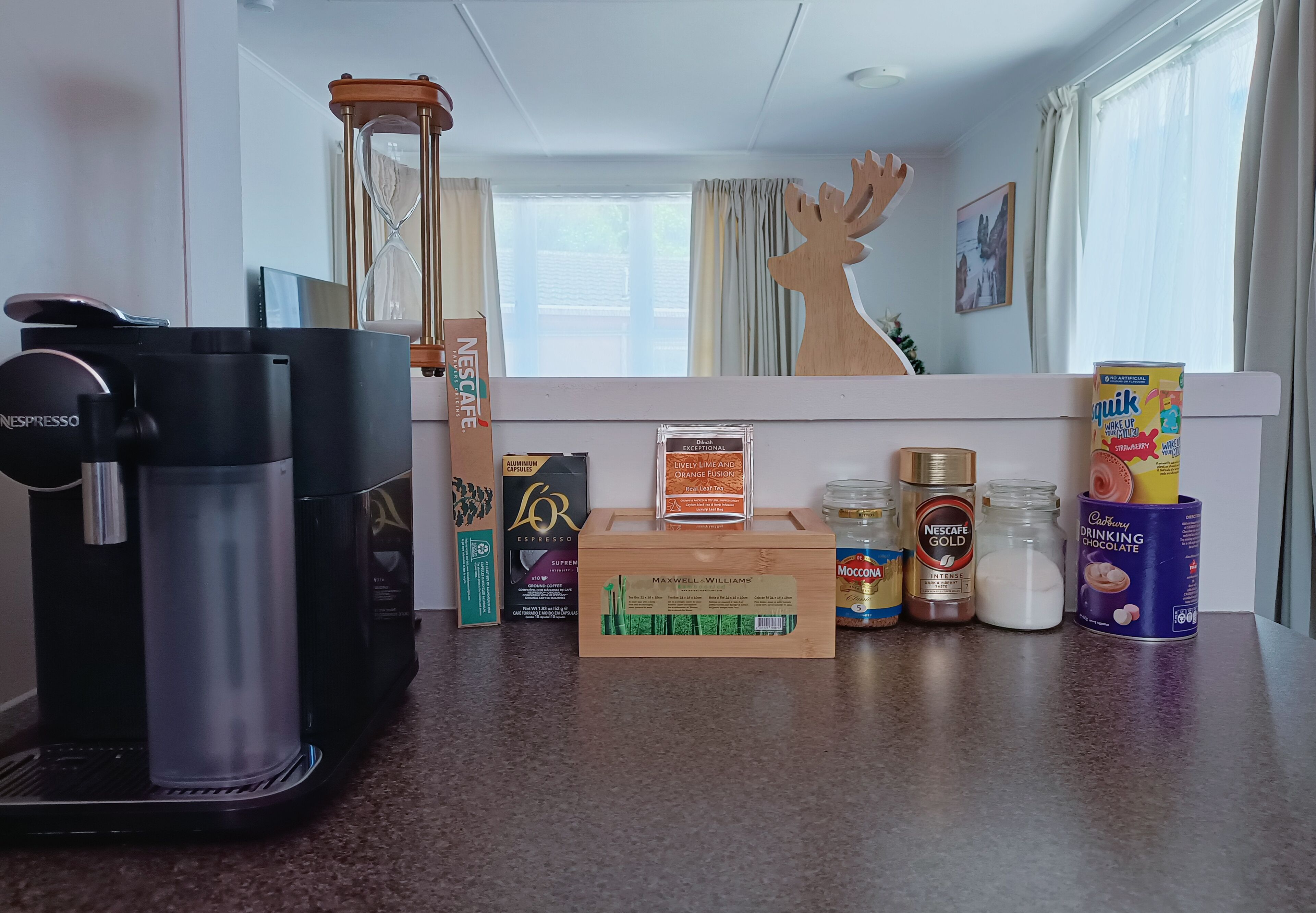 A kitchen counter with a Nespresso coffee machine, a wooden box labeled 'Maxwell Williams', and various coffee and chocolate products.