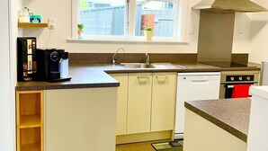 A compact kitchen with white cabinets, a window, a built-in stove, and a microwave. - Comfy & Sunny home in Wellington (Wellington)