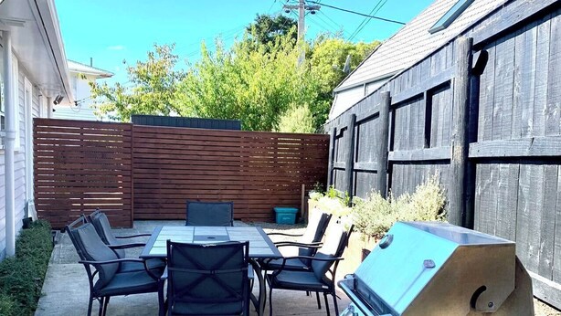 An outdoor patio with a table and chairs, a barbecue grill, and a wooden fence. - Comfy & Sunny home in Wellington (Wellington)