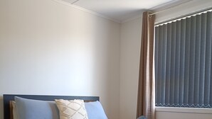 A neatly made bed with a blue and beige duvet, a wooden headboard, and a bedside table with a lamp. - Comfy & Sunny home in Wellington (Wellington)